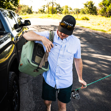The Padre light blue shirt worn outdoors by a man holding a cooler and fishing rod beside a car