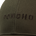 Close-up of a dark green fabric cap with the word "PONCHO" embroidered in dark brown thread across the front panel.