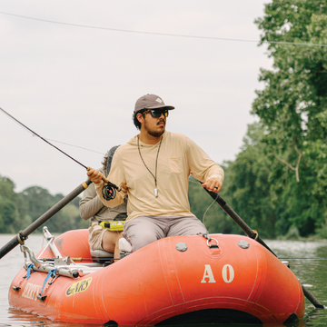 man casting fishing rod in boat wearing warm sand hoodie