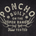 Text-based graphic on dark fabric with phrase "PONCHO BUILT ON THE OPEN RANGE Field TESTED" surrounded by antlers and two bullet casing icons.