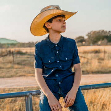 Boy sitting on a gate while on a farm in navy blue button down