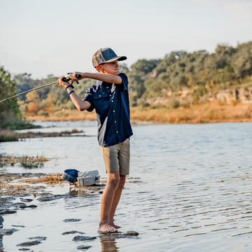 boy casting rod next to water wearing navy blue shirt