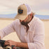 man fixing car with tan badge trucker hat