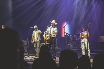 Musicians performing on a lit stage as audience silhouettes watch from the foreground