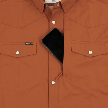 Close-up of a rust-colored shirt with snap buttons and a phone tucked into the concealed chest pocket of The 2005.