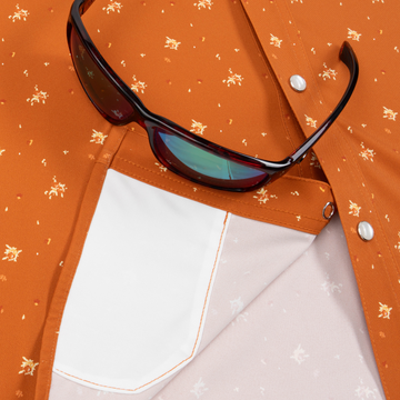 Close-up of an orange patterned shirt with a white inner pocket and sunglasses resting on it, featuring The 5th Year design.