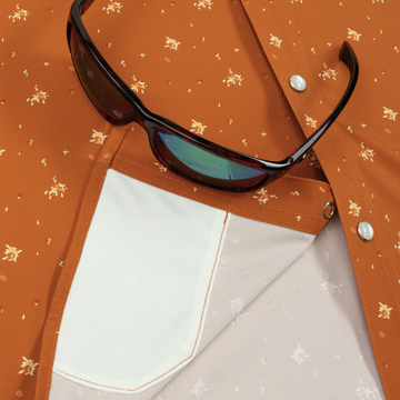 Close-up of rust-colored patterned shirt pocket with sunglasses resting on it, featuring The 5th Year design