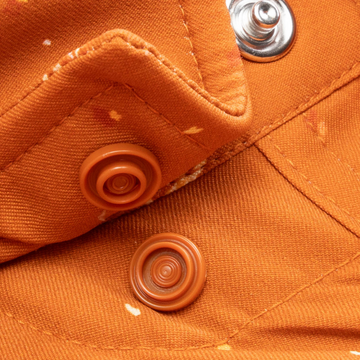 Close-up of orange fabric with snap buttons and stitching details on The 5th Year shirt.
