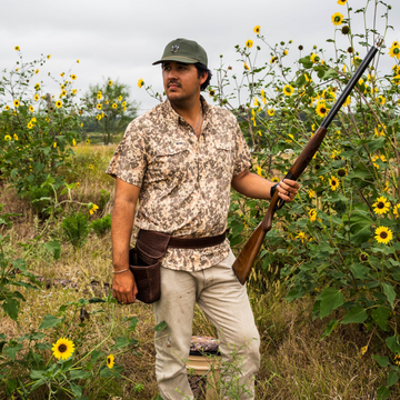 Man wearing The Abilene shirt outdoors holding a rifle among sunflowers