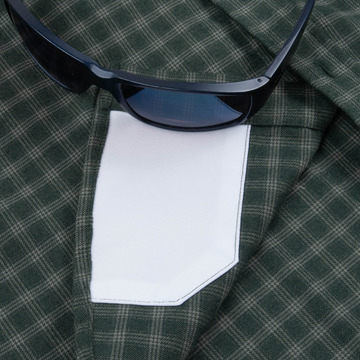 Close-up of The Acadia shirt showing green plaid fabric, white pocket detail, and black sunglasses resting on top