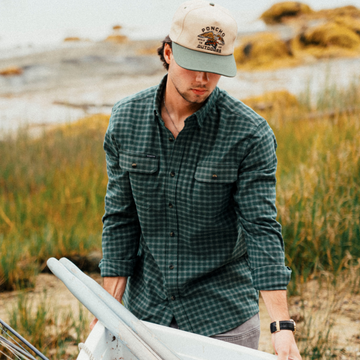 The Acadia teal and white plaid men's outdoor shirt with long sleeves and chest pockets by the shore