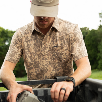 Man wearing a patterned short-sleeve shirt called The Armadillo outdoors while handling equipment in a truck bed