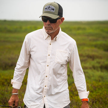 Man wearing sunglasses and a hat walking outdoors in a light checkered shirt called The Baja.