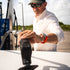 Man wearing sunglasses and a hat outdoors reaching to pump gas, dressed in The Baja shirt with subtle check pattern