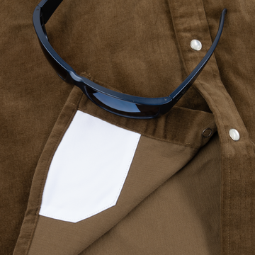 Close-up of The Barnhart shirt pocket with white interior and black sunglasses resting on brown fabric.