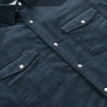 Close-up of dark blue The Barton Springs shirt with silver snap buttons and two front flap pockets, featuring Poncho Outdoors tag.
