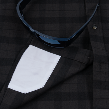 Close-up of The Black Canyon shirt featuring a dark checkered pattern with a white pocket and black sunglasses resting on it.
