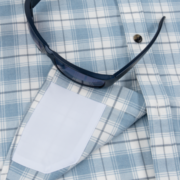 The Blue Bison shirt in light blue plaid fabric with a pair of dark blue sunglasses resting on it