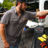 Man wearing The Bluetick shirt grilling corn and sausages outdoors near a truck
