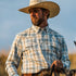 Man wearing The Brush Country shirt and cowboy hat outdoors, holding reins against a clear sky background