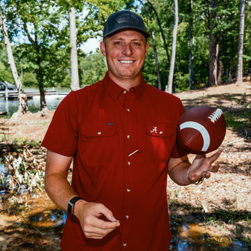 man tossing football wearing red alabama shirt