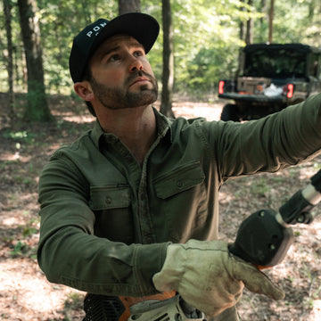 The Buck Snort green outdoor shirt worn by a man exploring a wooded trail beside an off road vehicle
