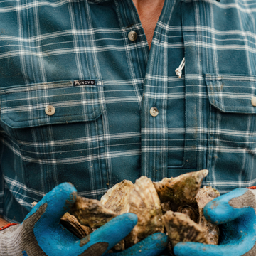 The Codfather plaid shirt from Poncho Outdoors holding fresh oysters outdoors