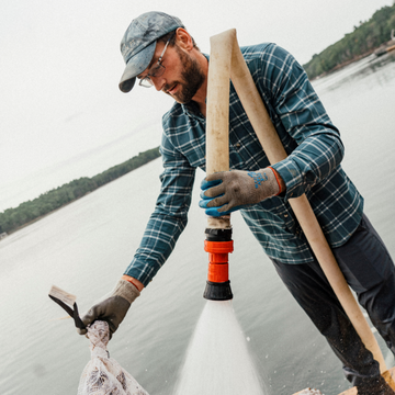 The Codfather plaid shirt worn by a worker using a water sprayer beside a lake