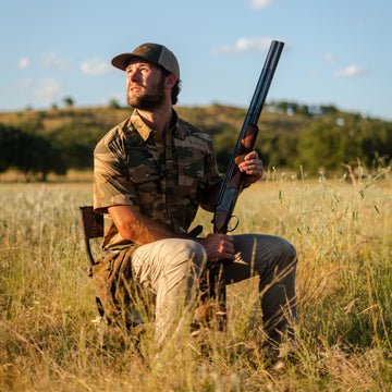 Man wearing The Cordoba shirt sitting in field holding shotgun