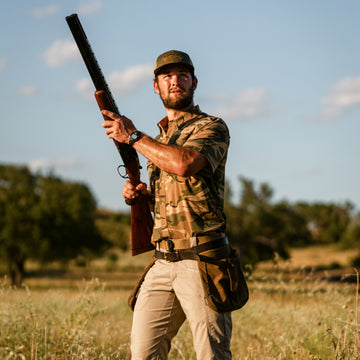 Man outdoors holding shotgun wearing The Cordoba camo shirt and utility belt