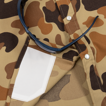 Close-up of The Delta Cowboy shirt in brown camo pattern featuring snap buttons and a white pocket holding sunglasses.