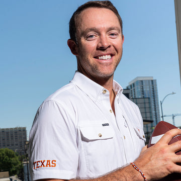 man holding football wearing white texas embroidered shirt