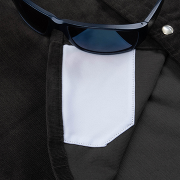 Close-up of a black shirt pocket with a white fabric detail and dark sunglasses resting on top, featuring The Dusty Burro design.