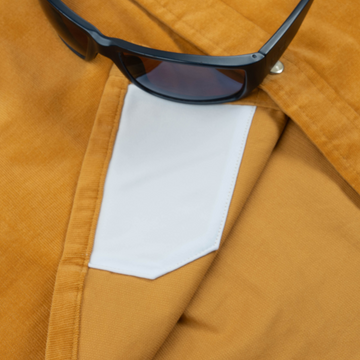 Close-up of The Enfield shirt pocket detail in mustard fabric with a pair of black sunglasses resting on top.