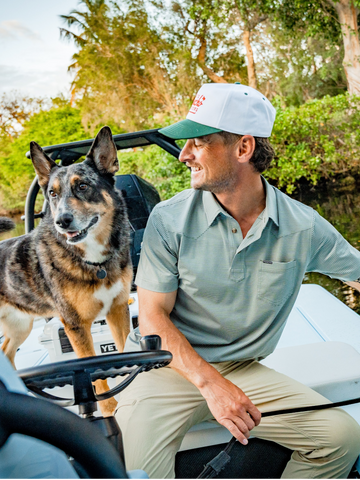 man wearing the farm to market performance polo with dog on boat