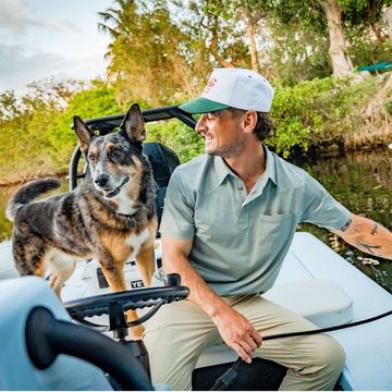 man wearing the farm to market performance polo with dog on boat