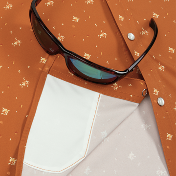 Close-up of "The Fourth and Five" shirt with a detailed pocket and folded fabric in warm brown tones, paired with black sunglasses.
