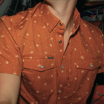 Close-up of a rust-colored short sleeve shirt with small floral print and snap buttons from The Fourth and Five.
