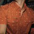 Close-up of a rust-colored short sleeve shirt with small floral print and snap buttons from The Fourth and Five.