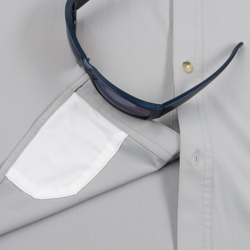 Close-up of The Grey Ghost shirt pocket holding a pair of dark sunglasses on light grey fabric.