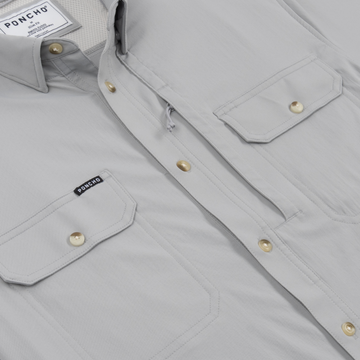 Close-up of a light grey outdoors shirt with brass buttons and pocket flaps, called The Grey Ghost.