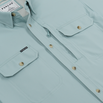 Close-up of a light blue outdoor shirt with buttoned chest pockets and a Poncho label on one pocket.