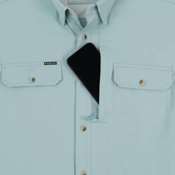 Light blue shirt with buttoned chest pockets, one pocket partially open holding a black smartphone.