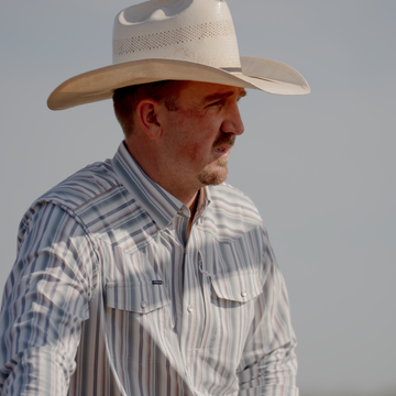 Man wearing a striped button-up shirt and a wide-brimmed hat outdoors showcasing The Hammer Down shirt.