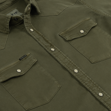 Close-up of The Hidalgo shirt in olive green with snap buttons and dual chest pockets, outdoors style.