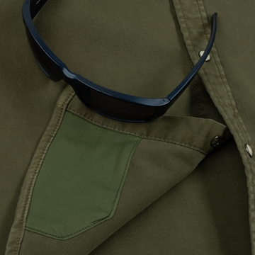 Close-up of The Hidalgo shirt pocket with a pair of dark sunglasses resting on olive green fabric.