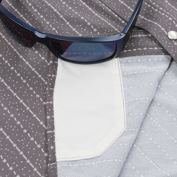 Close-up of a patterned shirt pocket detail with sunglasses resting on it, featuring The Camino design.