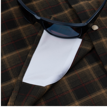Close-up of The John Colter shirt pocket detail with black sunglasses resting on the brown plaid fabric