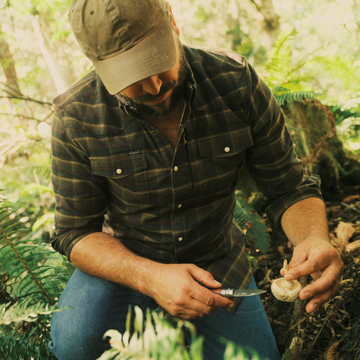 The John Colter black red and tan plaid mens outdoor shirt with chest pockets in a forest