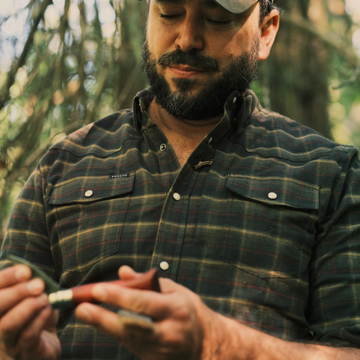 The John Colter Black, Red, and Tan Plaid men's outdoor shirt with snap chest pockets in a forest